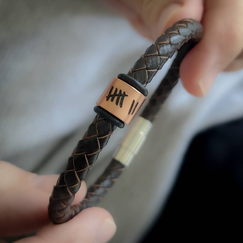 Pu&ograve; includere: Un braccialetto in pelle marrone con un perno in rame inciso con numeri romani. Il braccialetto ha una chiusura magnetica.
