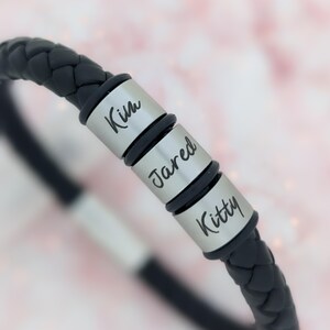 May include: Black leather bracelet with three silver beads engraved with the names "Kim", "Jared", and "Kitty".
