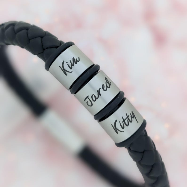 May include: Black leather bracelet with three silver beads engraved with the names "Kim", "Jared", and "Kitty".