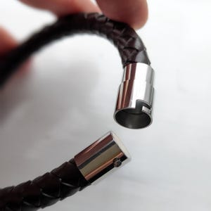 May include: A brown leather bracelet with a braided design and a silver magnetic clasp.