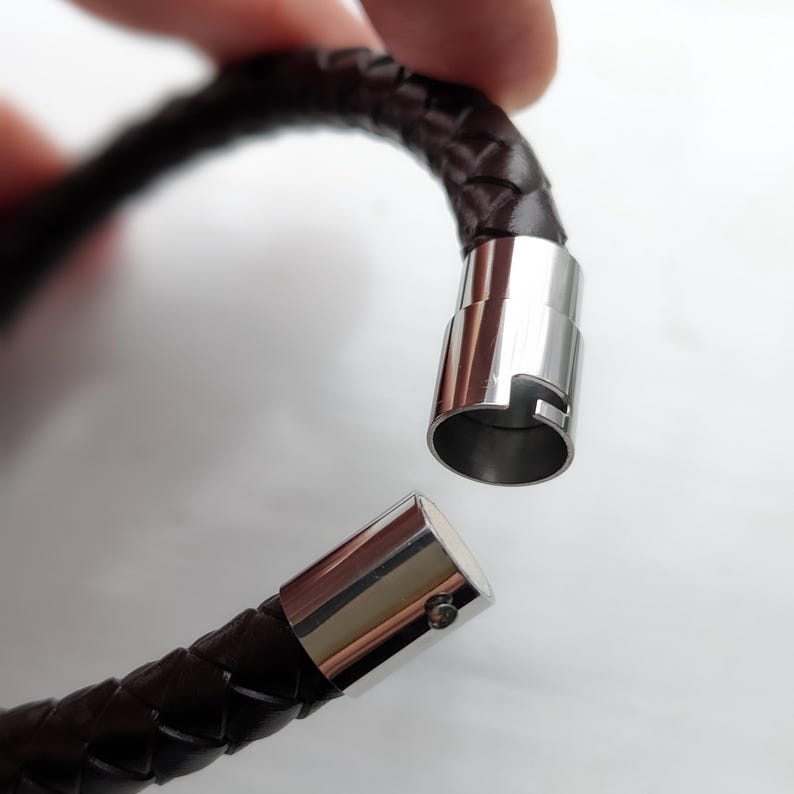 May include: A brown leather bracelet with a braided design and a silver magnetic clasp.