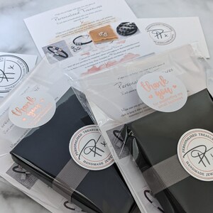 May include: Two black gift boxes with gray ribbon and a white sticker that says "Personalized Treasures" and "Handmade Jewelry". The boxes are wrapped in clear plastic and have a thank you sticker that says "Thank you for supporting my small business".
