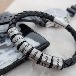 May include: Black leather bracelet with silver beads engraved with the names Harley, Harry, Sophie, Ioan, Owen, and Seren.
