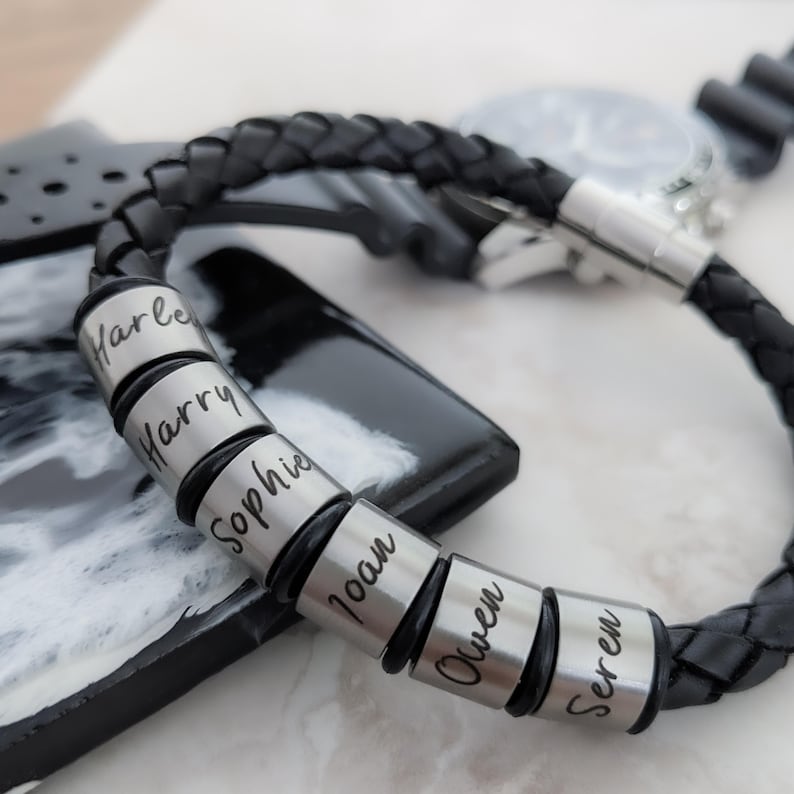 May include: Black leather bracelet with silver beads engraved with the names Harley, Harry, Sophie, Ioan, Owen, and Seren.