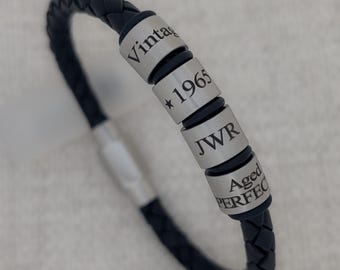May include: Black leather bracelet with silver beads. The beads are engraved with the text "Vintage", "* 1965", "JWR", and "Aged Perfect".