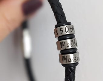 May include: Black leather bracelet with three silver beads. The beads are engraved with the text "It's 50th", "Molly", and "Maisy".