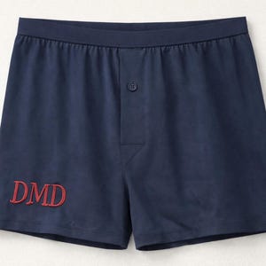 May include: Navy blue boxer shorts featuring an elasticized waistband, a central button fly, and the embroidered red letters DMD on the lower left side. The garment is constructed with a smooth fabric finish and a classic cut for everyday wear.