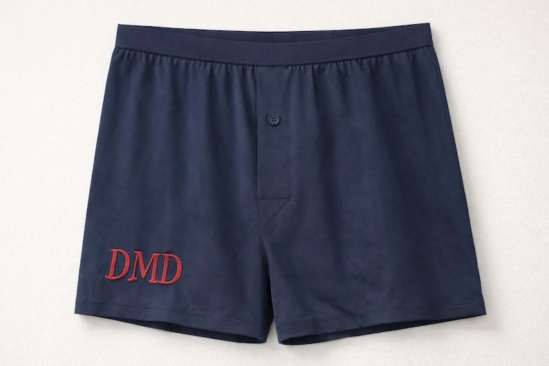 May include: Navy blue boxer shorts featuring an elasticized waistband, a central button fly, and the embroidered red letters DMD on the lower left side. The garment is constructed with a smooth fabric finish and a classic cut for everyday wear.