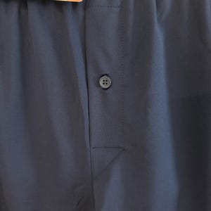 May include: A pair of dark blue boxer shorts featuring a central button closure on the fly. The waistband is elasticized and displays the text JOCKEY MICROFIBER FREEDOM. A product tag is attached to the top, showing a partial view of the garment.