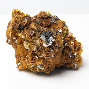 May include: A mineral specimen featuring a cluster of translucent, amber-colored, plate-like crystals embedded in a porous, reddish-brown matrix. The crystalline structure displays a metallic luster with scattered dark, opaque inclusions throughout.