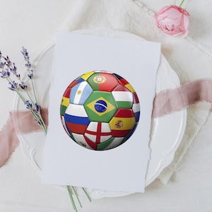 Puede incluir: Un bal&oacute;n de f&uacute;tbol con un patr&oacute;n multicolor compuesto por varias banderas nacionales, incluyendo Brasil, Argentina, Inglaterra, Espa&ntilde;a y Portugal, impreso en una tarjeta rectangular blanca con borde irregular, sobre un plato blanco.