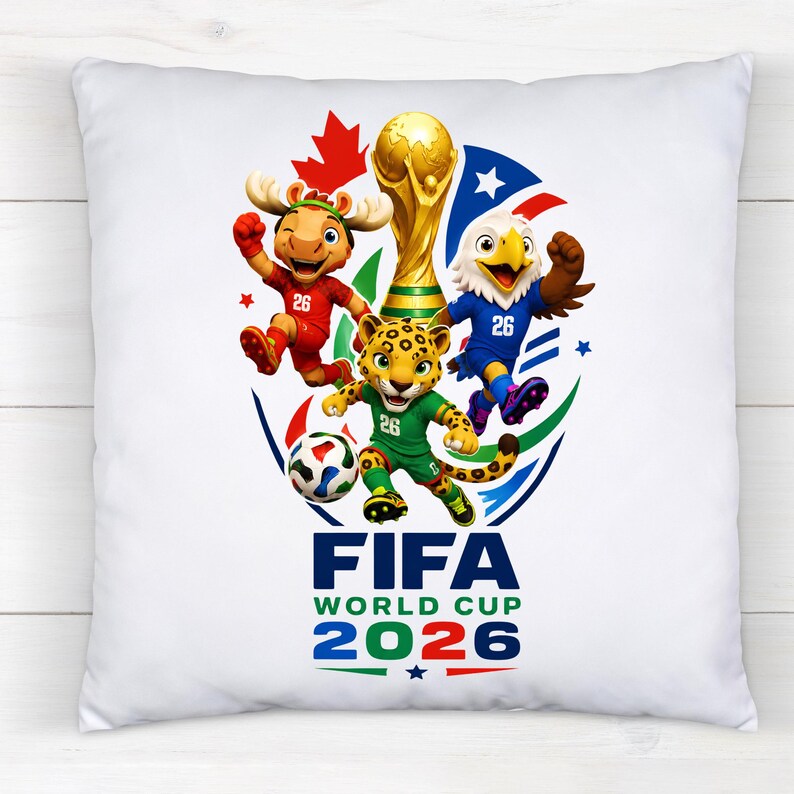 Puede incluir: Un coj&iacute;n cuadrado blanco con un gr&aacute;fico colorido del logotipo de la Copa Mundial de la FIFA 2026. El dise&ntilde;o incluye un trofeo dorado, un bal&oacute;n de f&uacute;tbol y tres mascotas con camisetas rojas, azules y verdes con el n&uacute;mero 26 y una hoja de arce.
