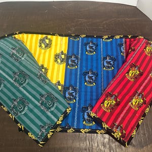 May include: A rectangular fabric runner featuring four vertical sections with striped patterns in green, yellow, blue, and red. Each section displays a repeating crest emblem and the text Harry Potter printed along the black fabric border.