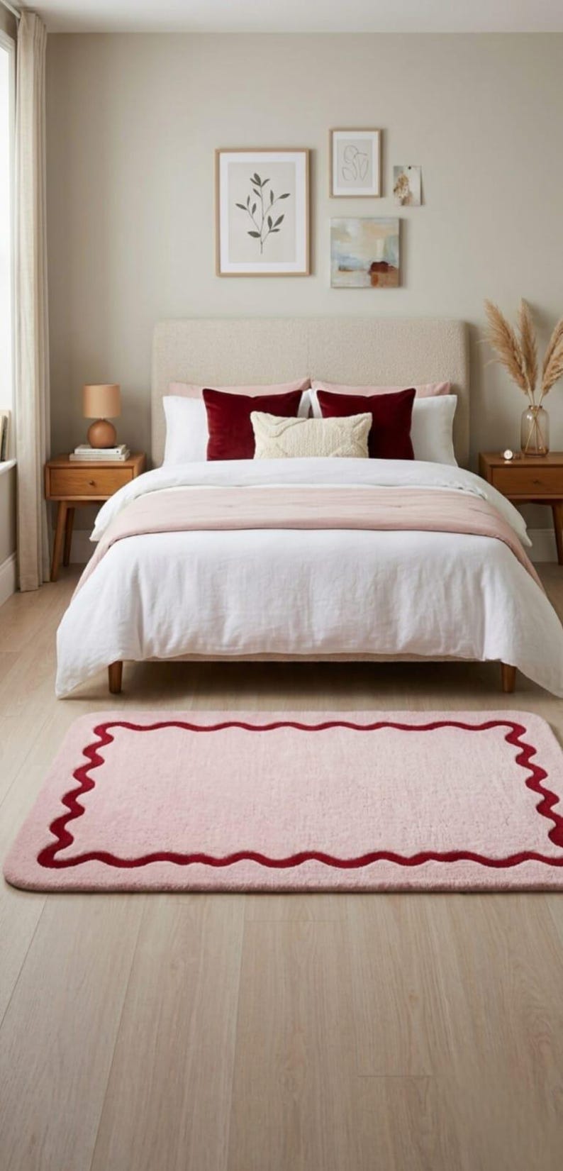 May include: A rectangular area rug featuring a soft light pink surface with a dark red scalloped border. The rug has rounded corners and a plush texture, positioned on a light-colored wooden floor in front of a bed with white and pink bedding.