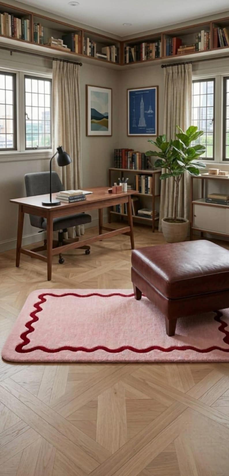 May include: A rectangular area rug featuring a soft pink center and a dark red wavy border. The rug is placed on a light-colored wooden floor with a herringbone pattern, positioned in front of a brown leather ottoman in a home office setting.
