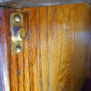 May include: Close-up of the inside of a wooden cabinet with a brass latch. The wood is a light brown color and has a grain pattern. The latch is attached to the wood with two screws.
