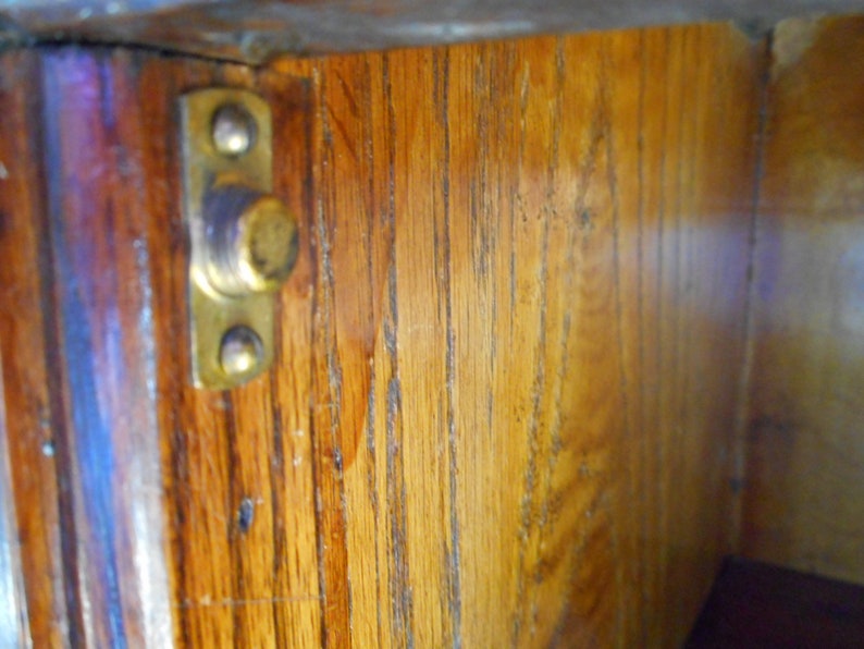 May include: Close-up of the inside of a wooden cabinet with a brass latch. The wood is a light brown color and has a grain pattern. The latch is attached to the wood with two screws.