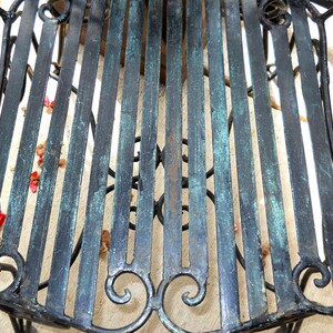 May include: A black metal chair with a green patina finish. The chair has a slatted seat and a decorative scroll design on the back.