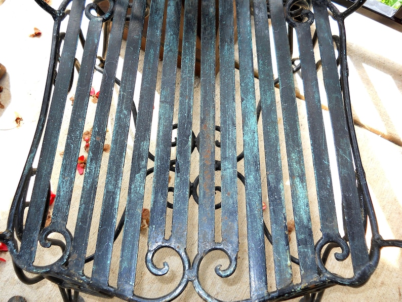 May include: A black metal chair with a green patina finish. The chair has a slatted seat and a decorative scroll design on the back.