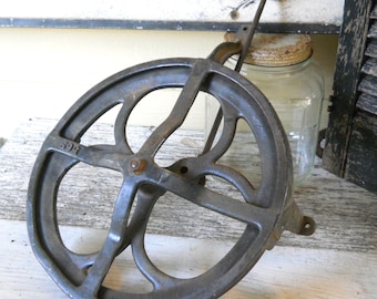 May include: A vintage cast iron pulley with a 599 stamped on the side. The pulley has a wheel with spokes and a metal arm attached to it.