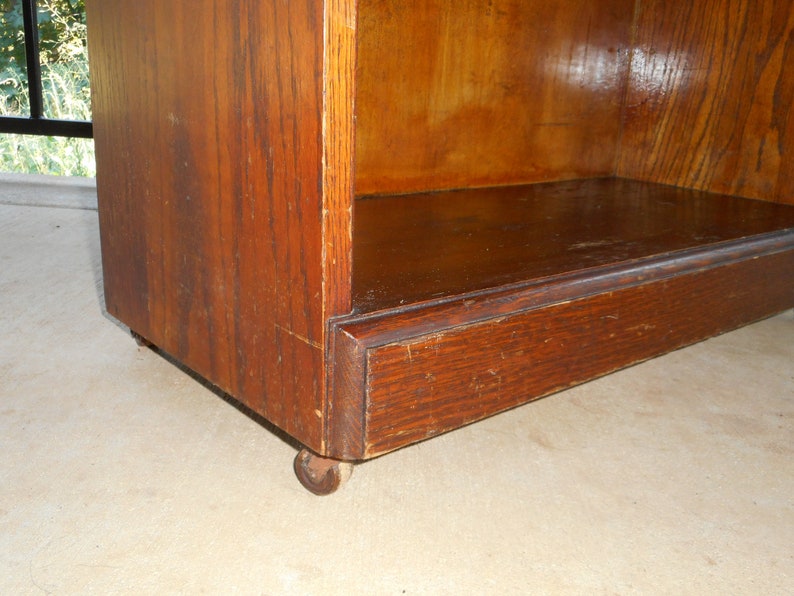 May include: A wooden bookcase with a single shelf and a dark brown finish. The bookcase has a simple design and is on wheels.