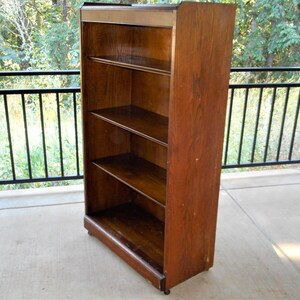 May include: A tall, wooden bookcase with four shelves. The bookcase is made of dark wood and has a simple design.