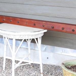 May include: A long, rectangular wooden shelf with a reddish-brown stain. The shelf has multiple evenly spaced metal hooks along the top. The shelf is mounted to a wall above a white wicker table.