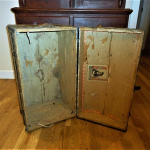 May include: An antique wooden suitcase with a floral patterned lining. The suitcase is open and empty, revealing the interior. The suitcase has a metal latch and hinges.