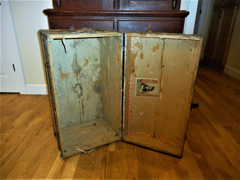 May include: An antique wooden suitcase with a floral patterned lining. The suitcase is open and empty, revealing the interior. The suitcase has a metal latch and hinges.