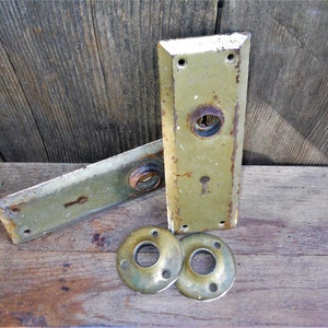 May include: Two antique door plates with keyholes and two matching round door knobs. The plates are made of metal and have a green patina. The knobs are brass.