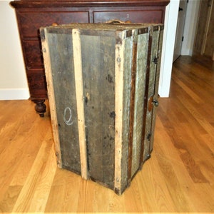 May include: A vintage wooden trunk with metal accents and a faded green paint finish. The trunk has a latch and hinges. The trunk is sitting on a wooden floor.