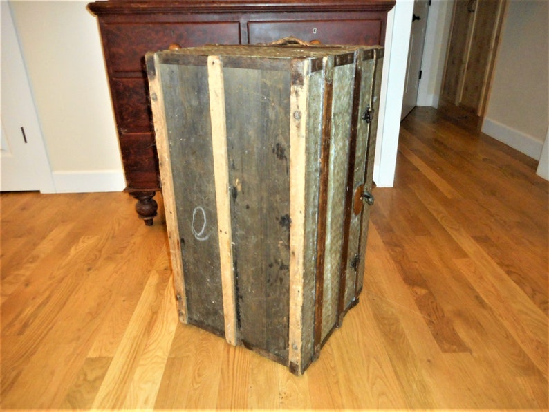 May include: A vintage wooden trunk with metal accents and a faded green paint finish. The trunk has a latch and hinges. The trunk is sitting on a wooden floor.