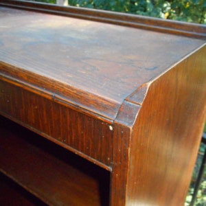 May include: A dark wood bookcase with multiple shelves. The bookcase has a simple design with a slightly rounded top edge.