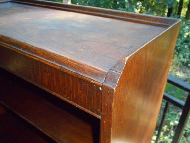 May include: A dark wood bookcase with multiple shelves. The bookcase has a simple design with a slightly rounded top edge.
