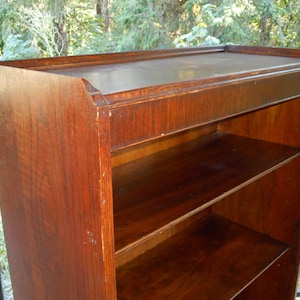 May include: A dark brown wooden bookcase with three shelves. The bookcase has a simple design with a slightly rounded top edge.