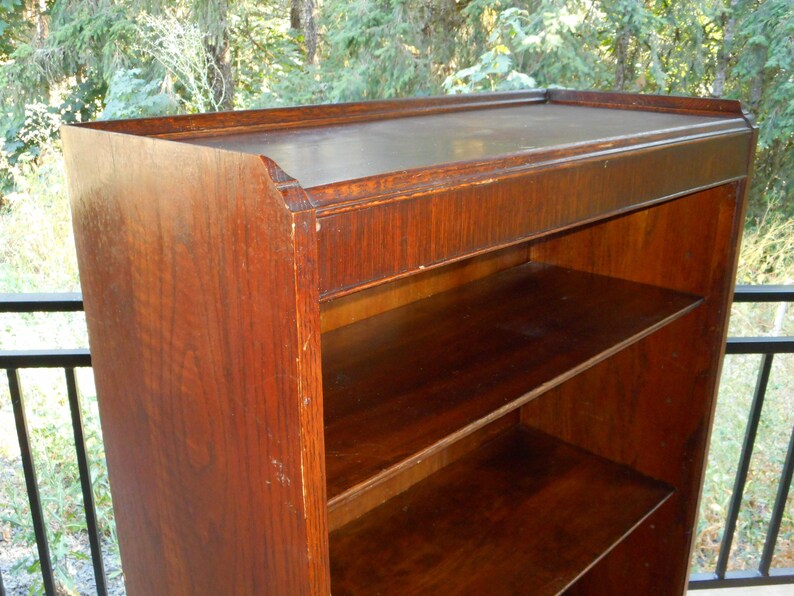 May include: A dark brown wooden bookcase with three shelves. The bookcase has a simple design with a slightly rounded top edge.