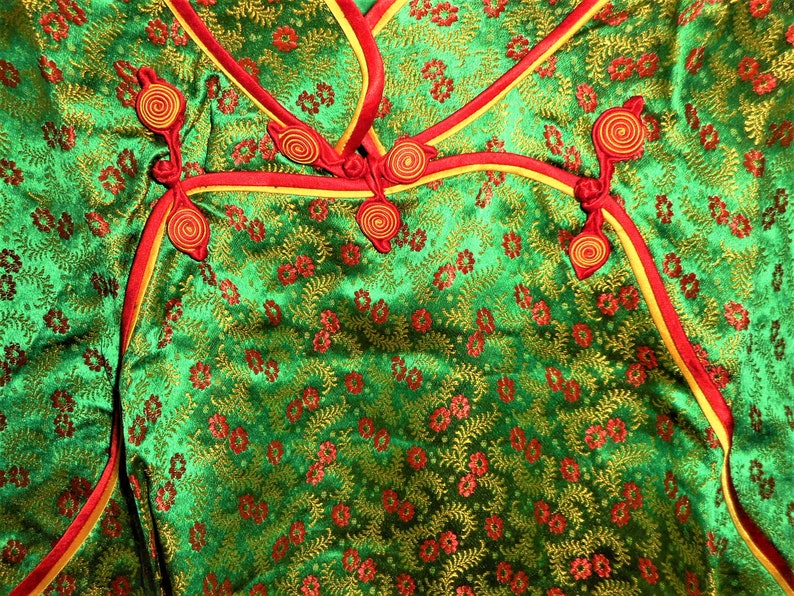 K&ouml;nnte beinhalten: Gr&uuml;ner Stoff mit Blumenmuster und rotem und goldenem Besatz. Der Stoff hat eine Reihe von dekorativen Knoten mit einem Spiralmuster.