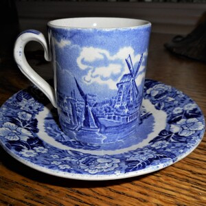 May include: A blue and white porcelain teacup and saucer set with a windmill and floral design.