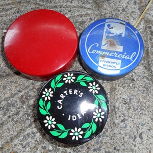 May include: Three round metal tins. One is red, one is blue with the text "Commercial Typewriter Ribbon", and one is black with a green and white floral design and the text "Carter's Idea".