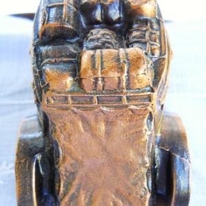 May include: A bronze-coloured metal figurine of a horse-drawn carriage with a detailed design. The carriage is filled with luggage and the wheels are visible.