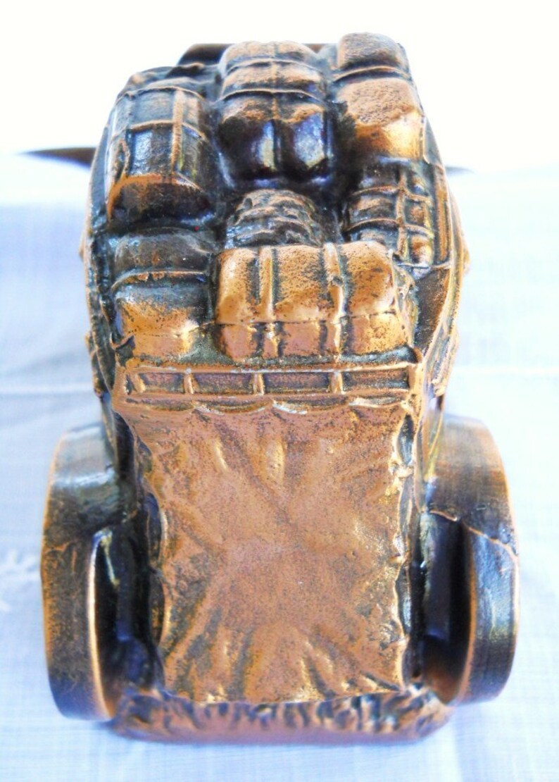 May include: A bronze-coloured metal figurine of a horse-drawn carriage with a detailed design. The carriage is filled with luggage and the wheels are visible.