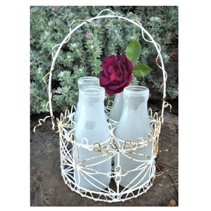 May include: A white wire milk bottle holder with four frosted glass milk bottles and a single red rose.