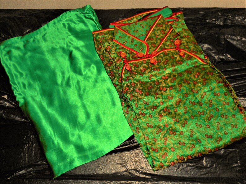 K&ouml;nnte beinhalten: Eine gr&uuml;ne Satinrobe mit Blumenmuster und rotem Besatz. Die Robe hat einen Mandarinkragen und Kn&ouml;pfe.