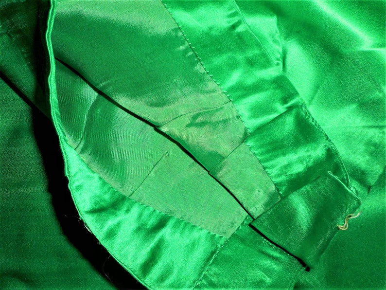 K&ouml;nnte beinhalten: Nahaufnahme des Innenfutters eines Kleidungsst&uuml;cks aus gr&uuml;nem Satin. Der Stoff ist &uuml;ber sich selbst gelegt und zeigt die N&auml;hte und die glatte Textur des Satins.