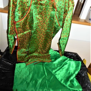 K&ouml;nnte beinhalten: Ein gr&uuml;nes Seidenkleid im chinesischen Stil mit goldenen und roten Blumenstickereien. Das Kleid hat einen Mandarin-Kragen, lange &Auml;rmel und einen passenden gr&uuml;nen Seidenrock.