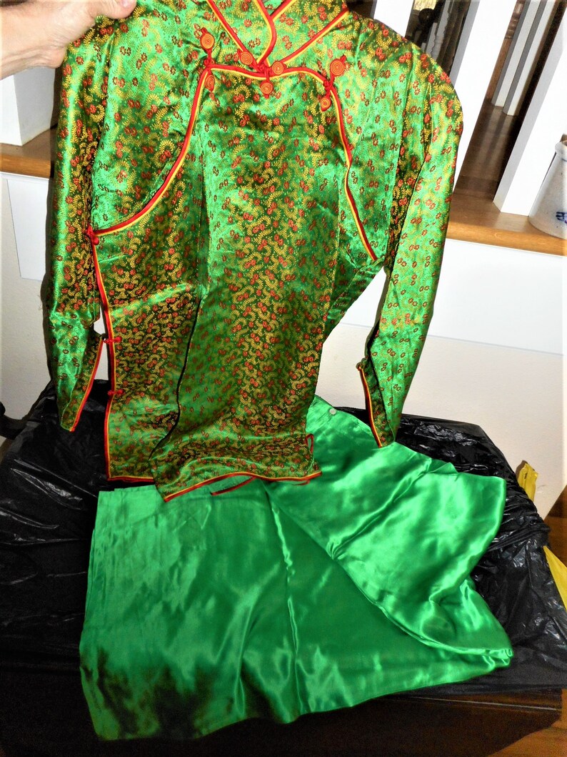 K&ouml;nnte beinhalten: Ein gr&uuml;nes Seidenkleid im chinesischen Stil mit goldenen und roten Blumenstickereien. Das Kleid hat einen Mandarin-Kragen, lange &Auml;rmel und einen passenden gr&uuml;nen Seidenrock.
