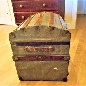 May include: A vintage, weathered, metal and wood travel trunk with a domed lid and brass hardware. The trunk is in a worn condition with visible scratches and dents.
