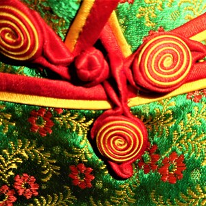 K&ouml;nnte beinhalten: Nahaufnahme eines gr&uuml;nen Stoffes mit einem goldenen und roten Blumenmuster. Der Stoff hat rote und goldene Kn&ouml;pfe mit einem Spiralmuster.