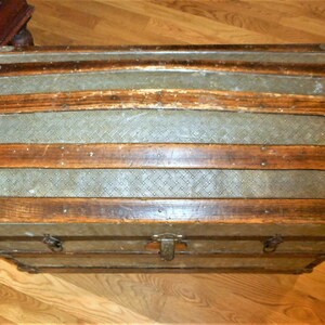 May include: A vintage wooden and metal travel trunk with a diamond pattern on the lid. The trunk has a brass latch and hinges.