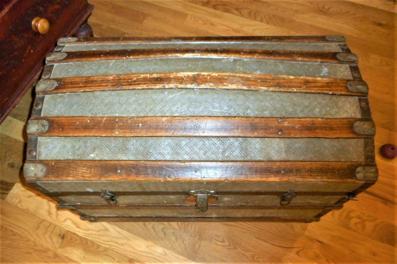 May include: A vintage wooden and metal travel trunk with a diamond pattern on the lid. The trunk has a brass latch and hinges.